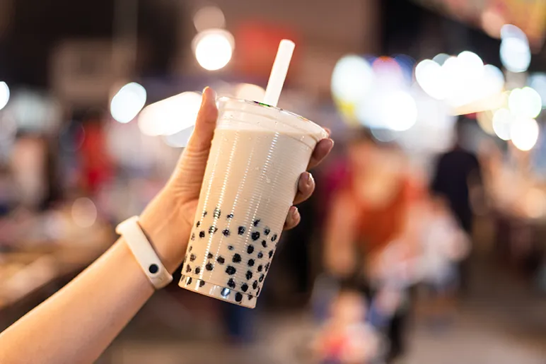Hand holding a container of bubble tea in front of a blurred street scene