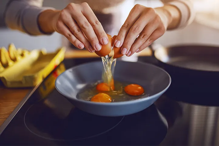 A woman's hands cracking an egg into a blue bowl where three eggs have already been opened.