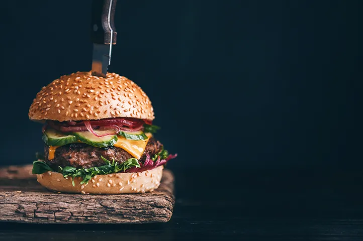 A burger served on a wooden board with a knife pushed into it