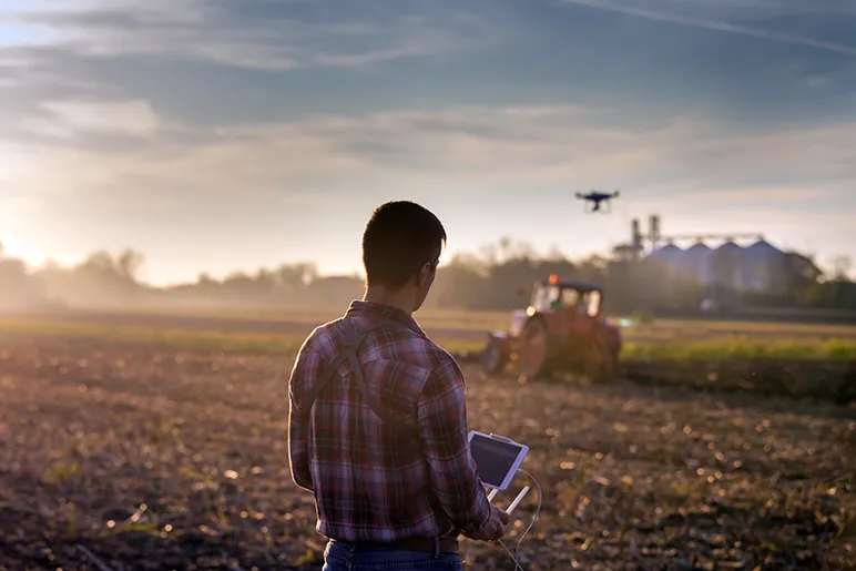 Man using drone to analyse tractor ploughing field in farm