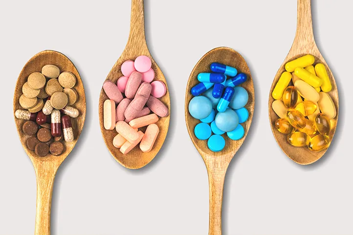 Four wooden spoons containing various vitamin supplements