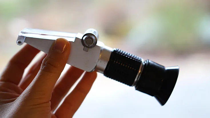 A hand holding a hand-held refractometer used for measuring the water content of honey